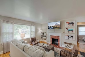 A living room with a sofa, armchairs, a fireplace, a TV, and artwork on the wall.