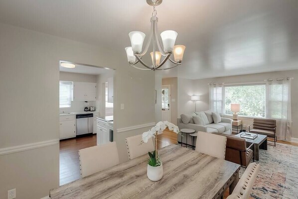 A dining area with a wooden table, chairs, a chandelier, and a potted orchid.