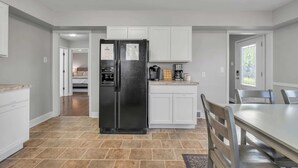 Una cocina con armarios blancos, un refrigerador negro, una cafetera y una mesa de comedor con sillas.