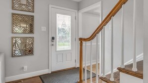 Un pasillo con escalera de madera, una puerta blanca con ventanal y paneles decorativos en las paredes.