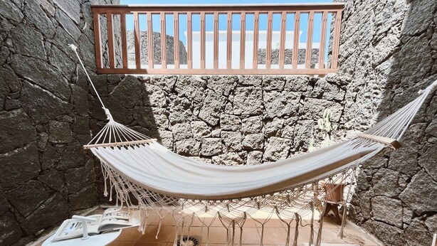A hammock in a stone-walled courtyard with a tiled floor, a white table, and a wooden bench. - Casa Moci (Playa Blanca)