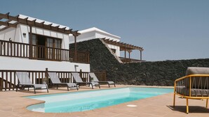 A pool area with lounge chairs and a stone wall. - Casa Moci (Playa Blanca)