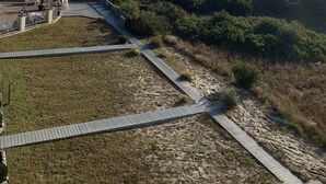Een kustlandschap met een strand, een houten looppad en een grasveld met begroeiing.
