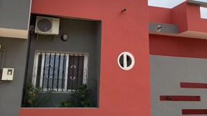 Un bâtiment moderne à la façade rouge et grise, doté d’une fenêtre avec des barreaux métalliques et d’un appareil de climatisation.
