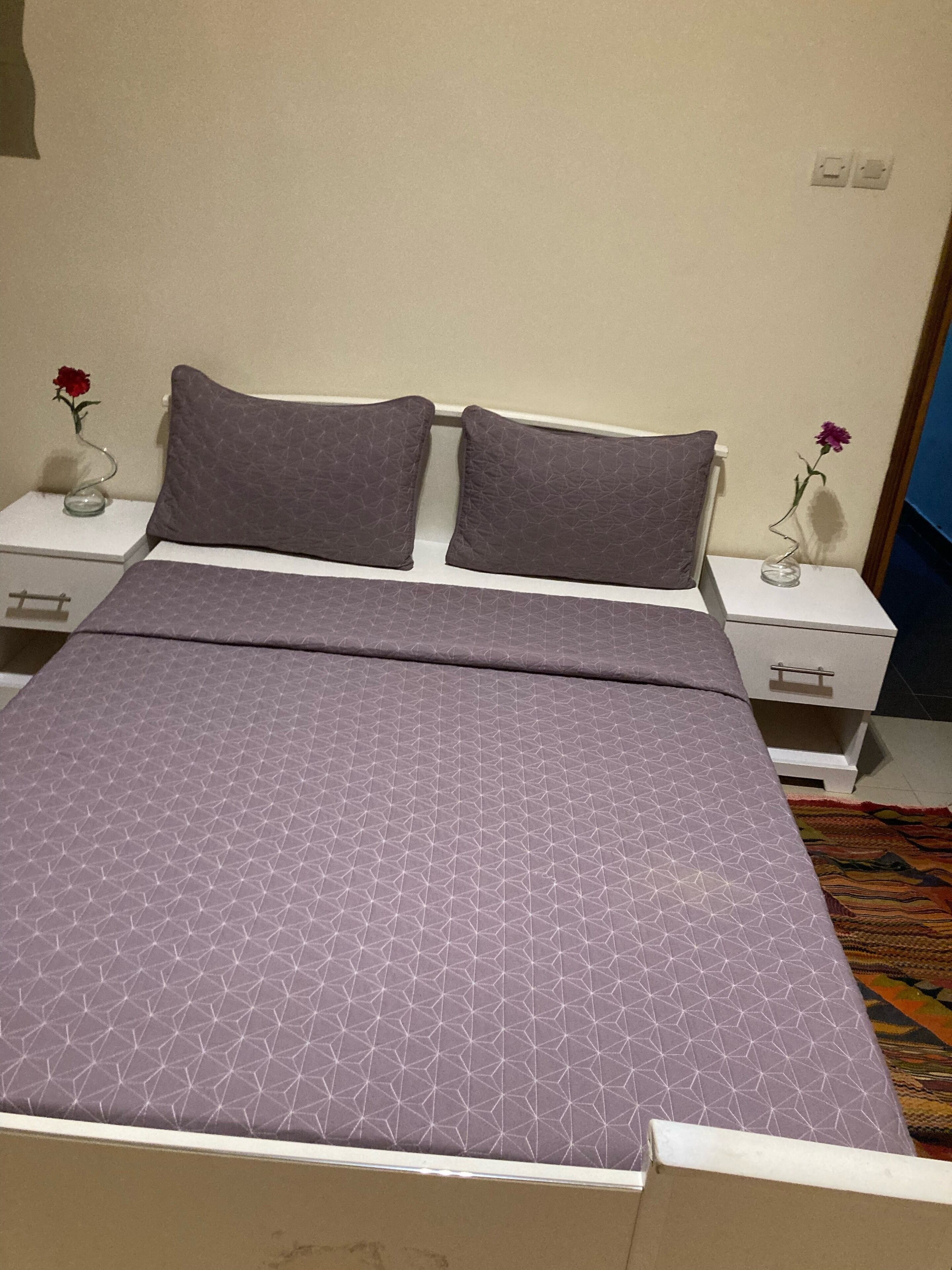 A neatly made bed with a geometric patterned bedspread, two matching pillows, and a nightstand with a vase of flowers.