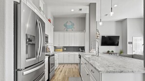 A modern kitchen with stainless steel appliances, white cabinetry, a herringbone backsplash, and a large island with a marble countertop.