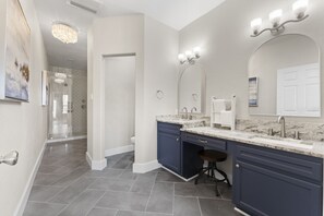 A modern bathroom with dark blue cabinets, a marble countertop, and a large mirror with lights. - Game Room-Beach Views-Incredible Breeze-Sleeps 14- Child Friendly (Bolivar Peninsula)
