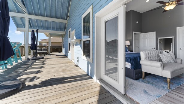 A covered outdoor deck with a sofa and a ceiling fan, leading to a room with a bed and a window.