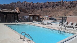 A swimming pool with a mountain backdrop, sun loungers, and a fenced area. - Beautiful Moab Townhome (moab)