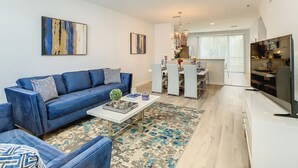 A modern living room with a blue sofa, a coffee table, and a dining area with a chandelier. - Vista Cay Townhouses by Casiola (Orlando)