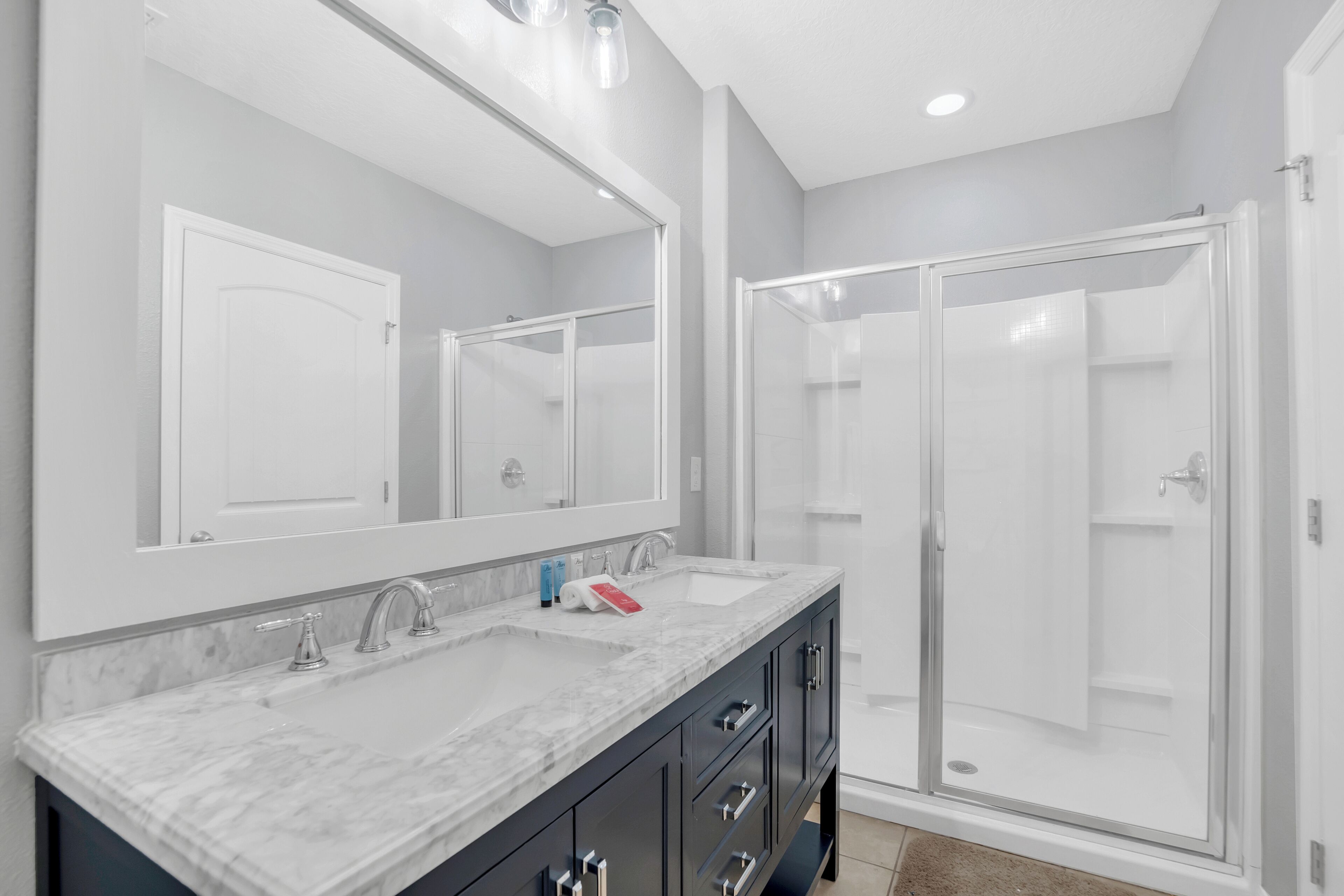 A bathroom with a double sink vanity, a large mirror, and a glass-enclosed shower.