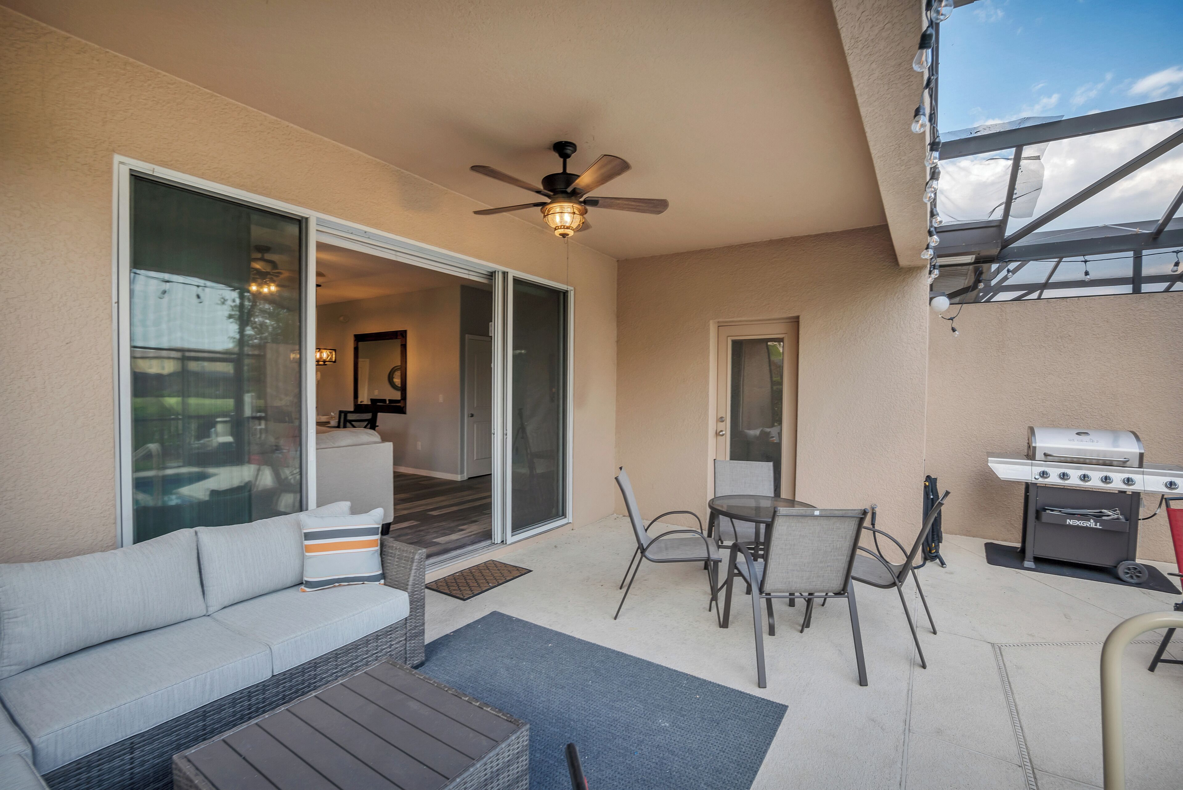 A patio with a sofa, chairs, a grill, and a ceiling fan.