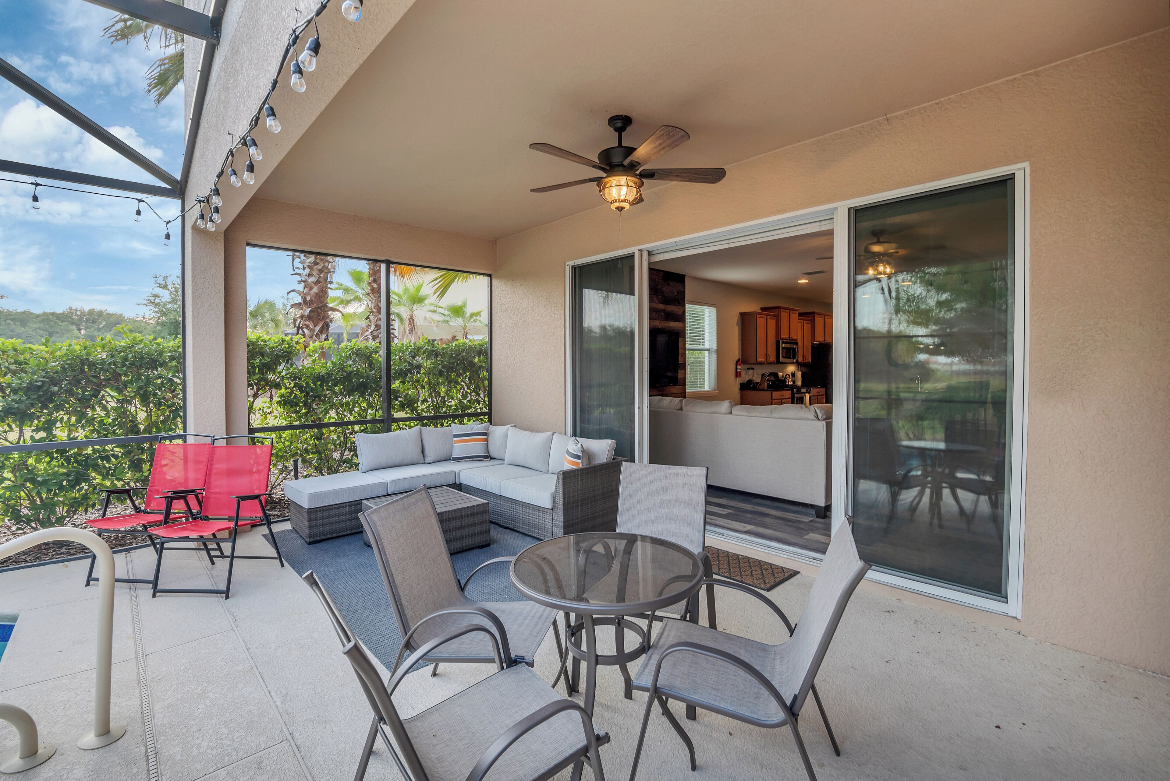 A covered outdoor patio with a glass balustrade, a ceiling fan, and a seating area with a sofa and chairs.