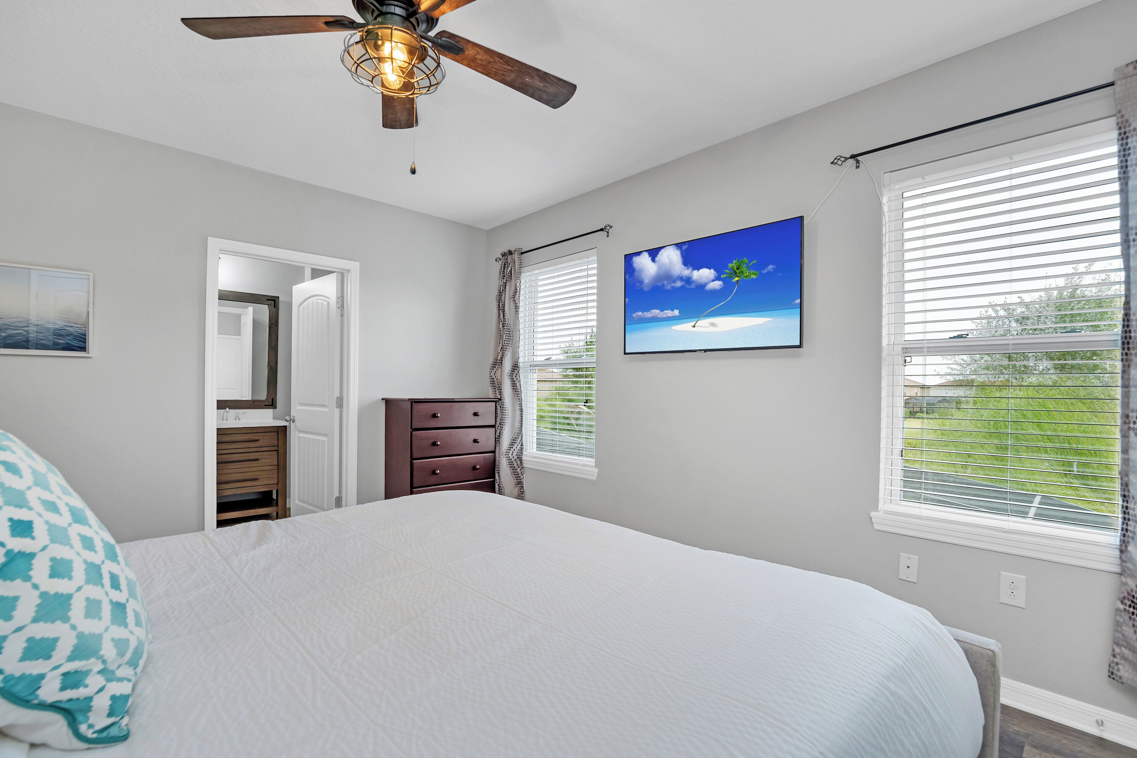 A bedroom with a bed, a ceiling fan, a TV, and a window with blinds.