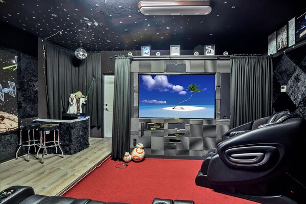 A room with a large flat-screen TV on the wall, a bar area with stools, and a red carpet. - 8897 Qin Loop (Kissimmee)