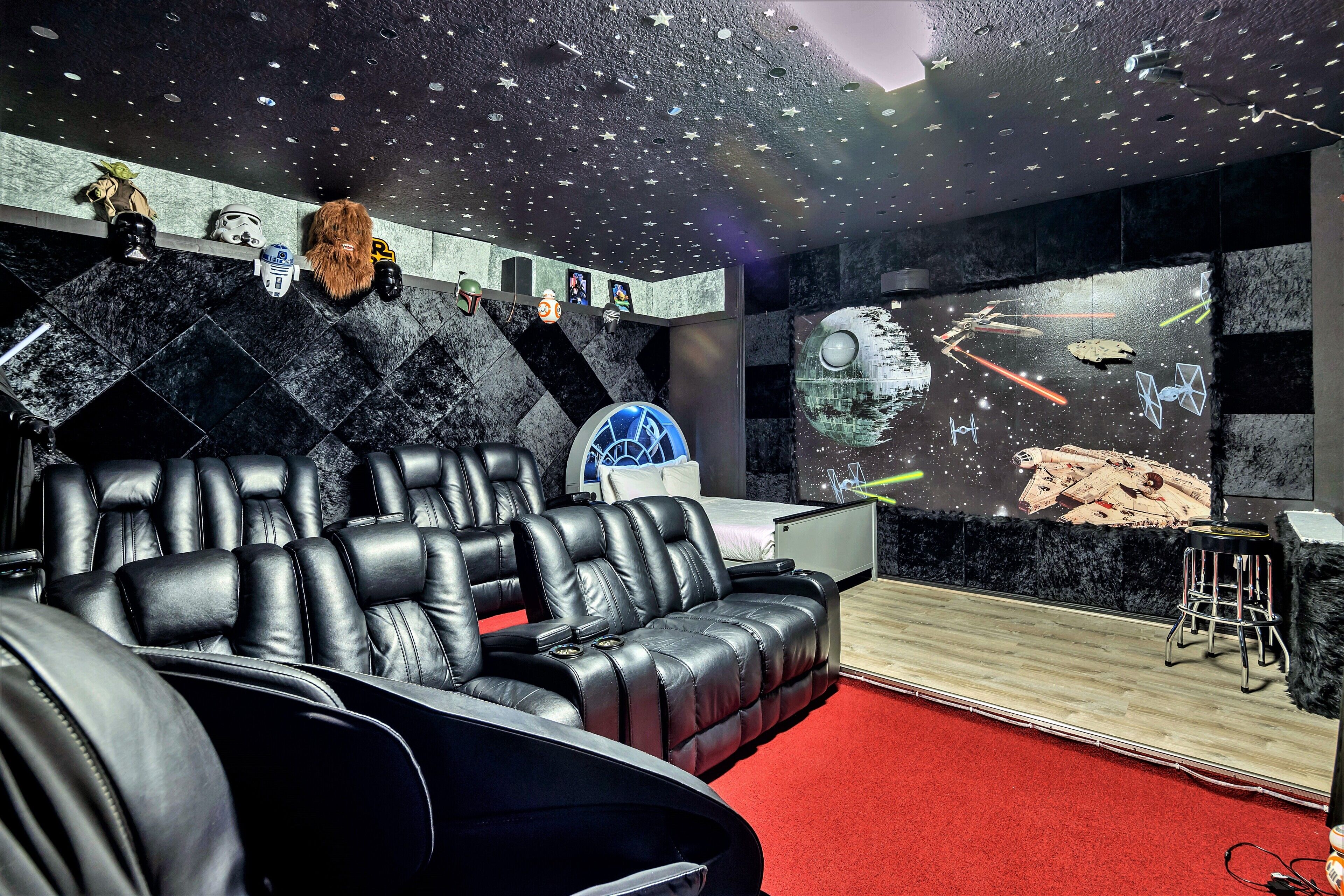 A room with a starry ceiling, a large screen displaying space-themed visuals, and a black leather sofa.