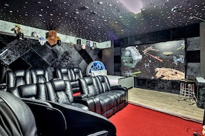 A room with a starry ceiling, a large screen displaying space-themed visuals, and a black leather sofa.