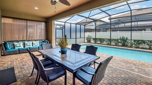 Eine überdachte Terrasse mit Pool, Esstisch und Sitzgelegenheiten.
