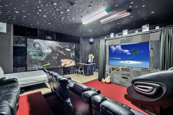 A home theater with a large screen, reclining chairs, a projector, and a starry ceiling.
