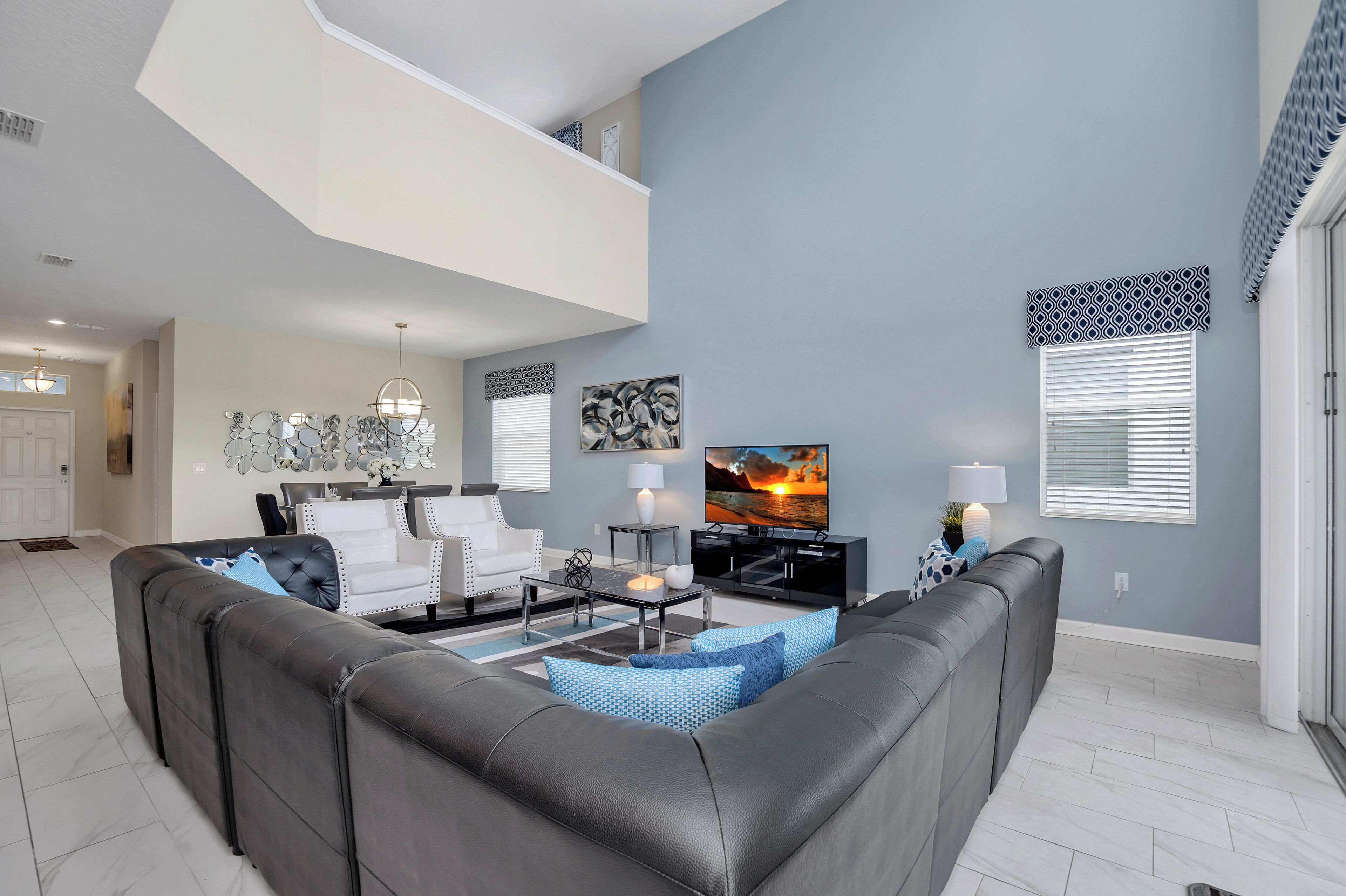 A modern living room with a sectional sofa, a flat-screen TV, and a dining area with a chandelier.
