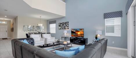 A modern living room with a sectional sofa, a flat-screen TV, and a dining area with a chandelier.