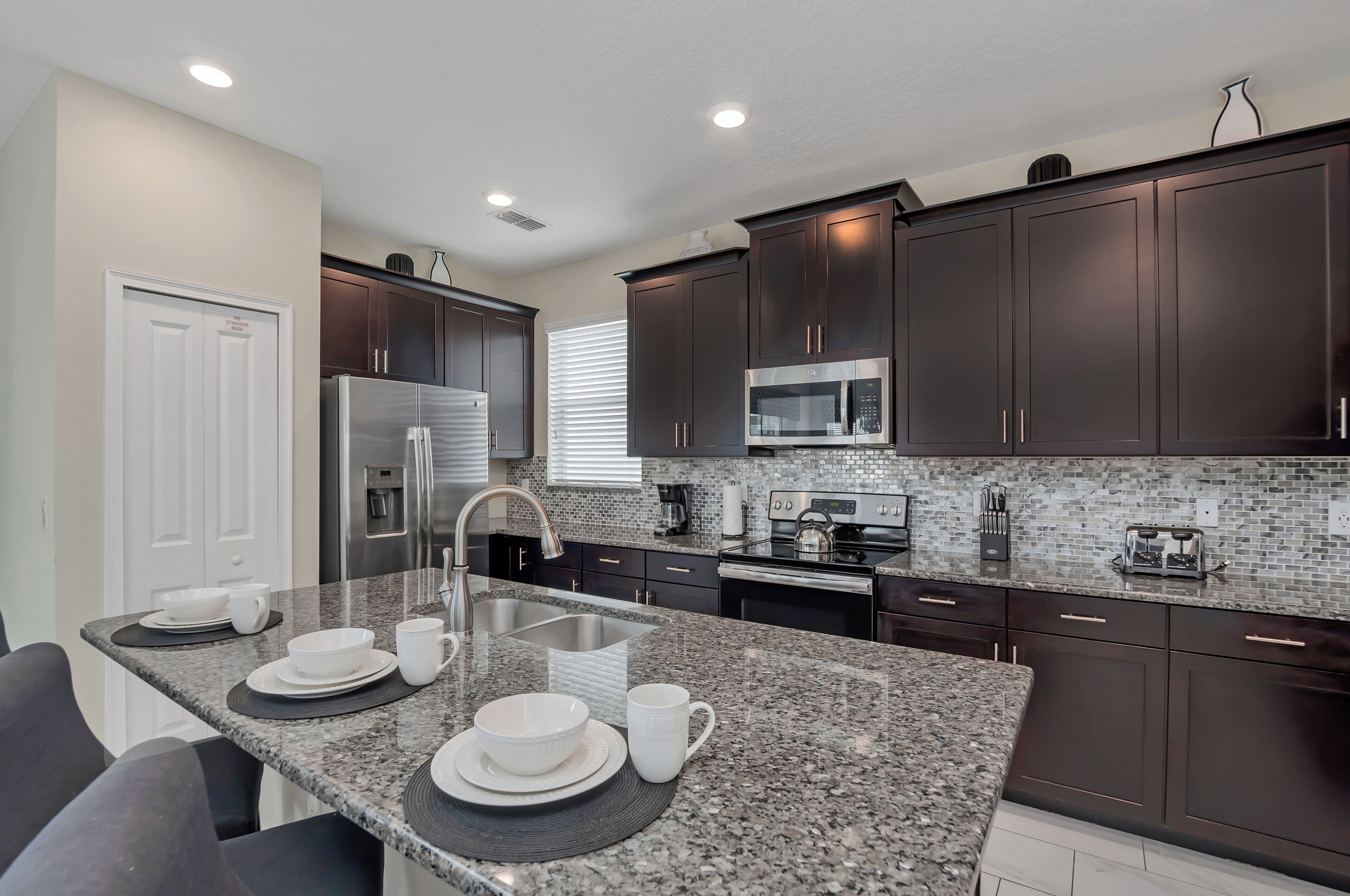 A modern kitchen with dark wood cabinets, stainless steel appliances, and a granite countertop.