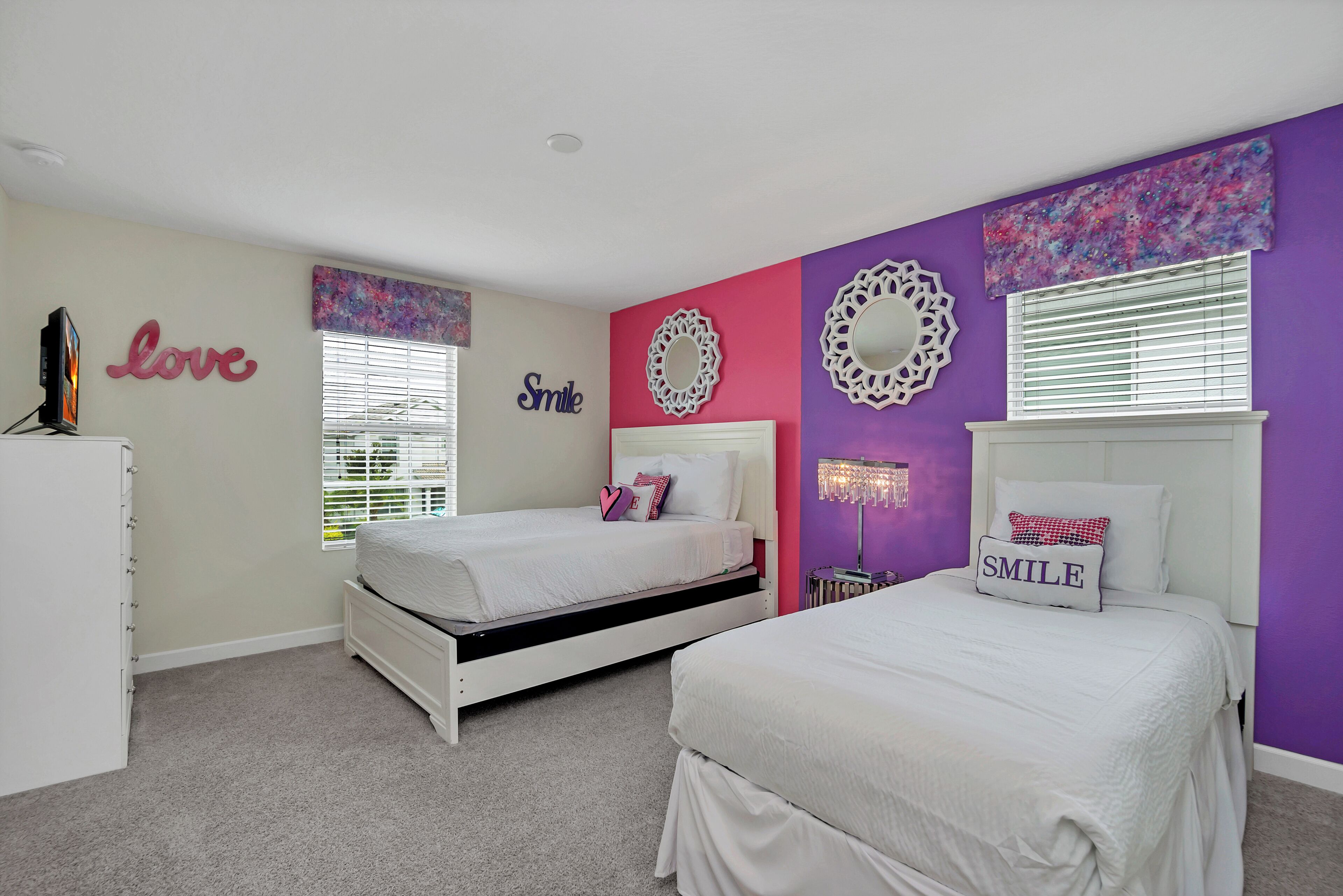 A bedroom with two beds, a dresser, and decorative wall art.