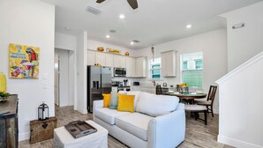 A modern kitchen with white cabinets, stainless steel appliances, and a dining area with a table set for four. - Margaritaville Cottage, Private Pool, Near Disney! (Kissimmee)
