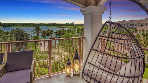 A balcony with a view of a lake, a hanging chair, and two lanterns.