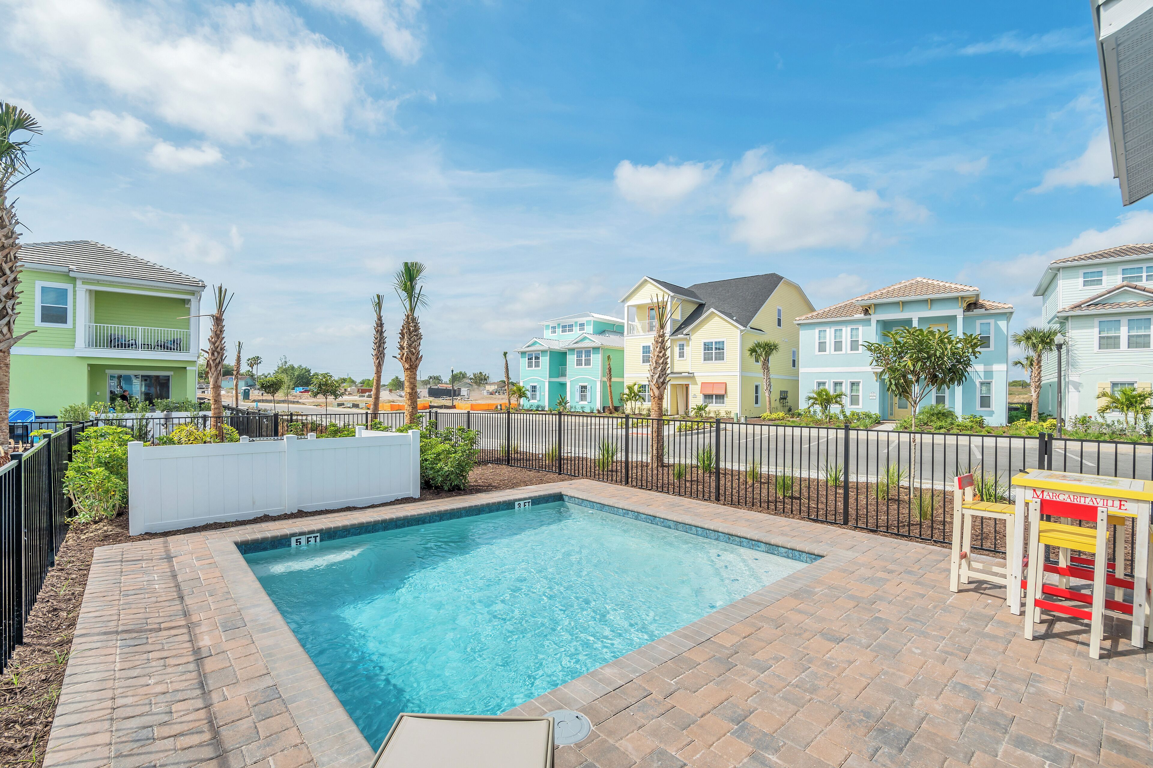 A swimming pool with a brick border, surrounded by a fence and palm trees.