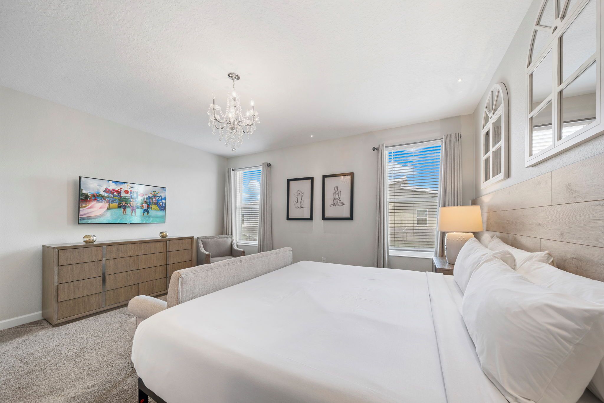 Une chambre à coucher avec un grand lit, une commode, une chaise, un téléviseur et des œuvres d’art encadrées accrochées au mur.