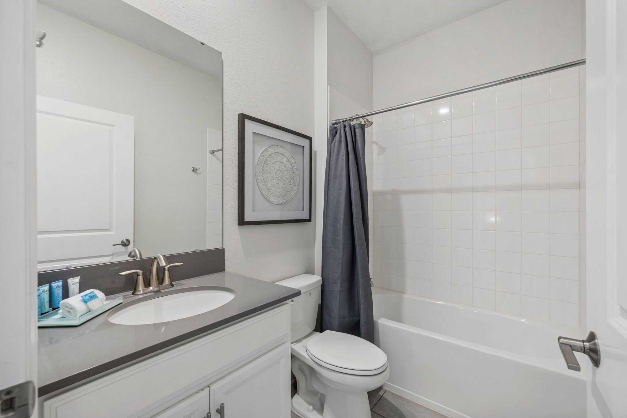 Een badkamer met een wit wastafelmeubel, toilet, bad en douchegordijn.