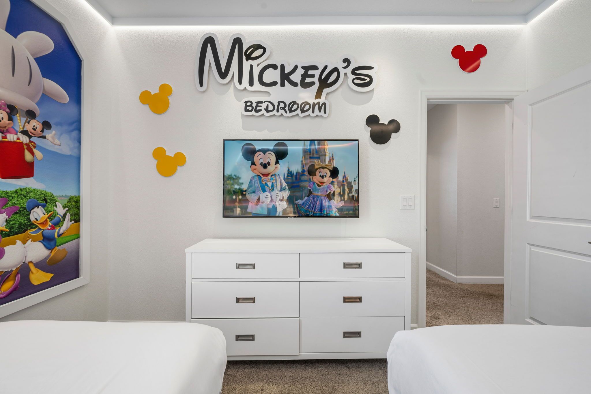 Ein Schlafzimmer im Mickey-Stil mit Wandgemälde, einem Flachbildfernseher und einer weißen Kommode.