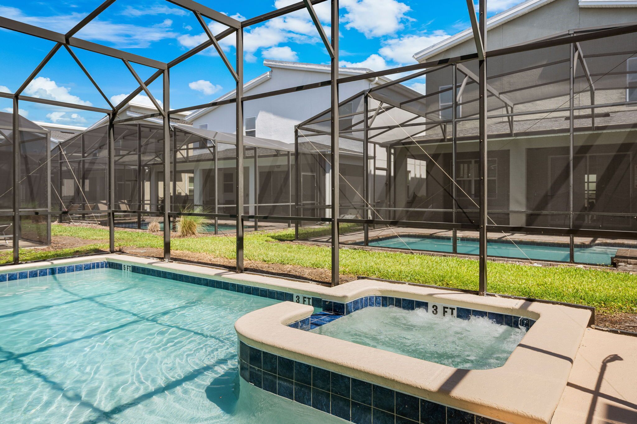 Een zwembad met een jacuzzi, omringd door een overdekt terras met uitzicht op huizen.