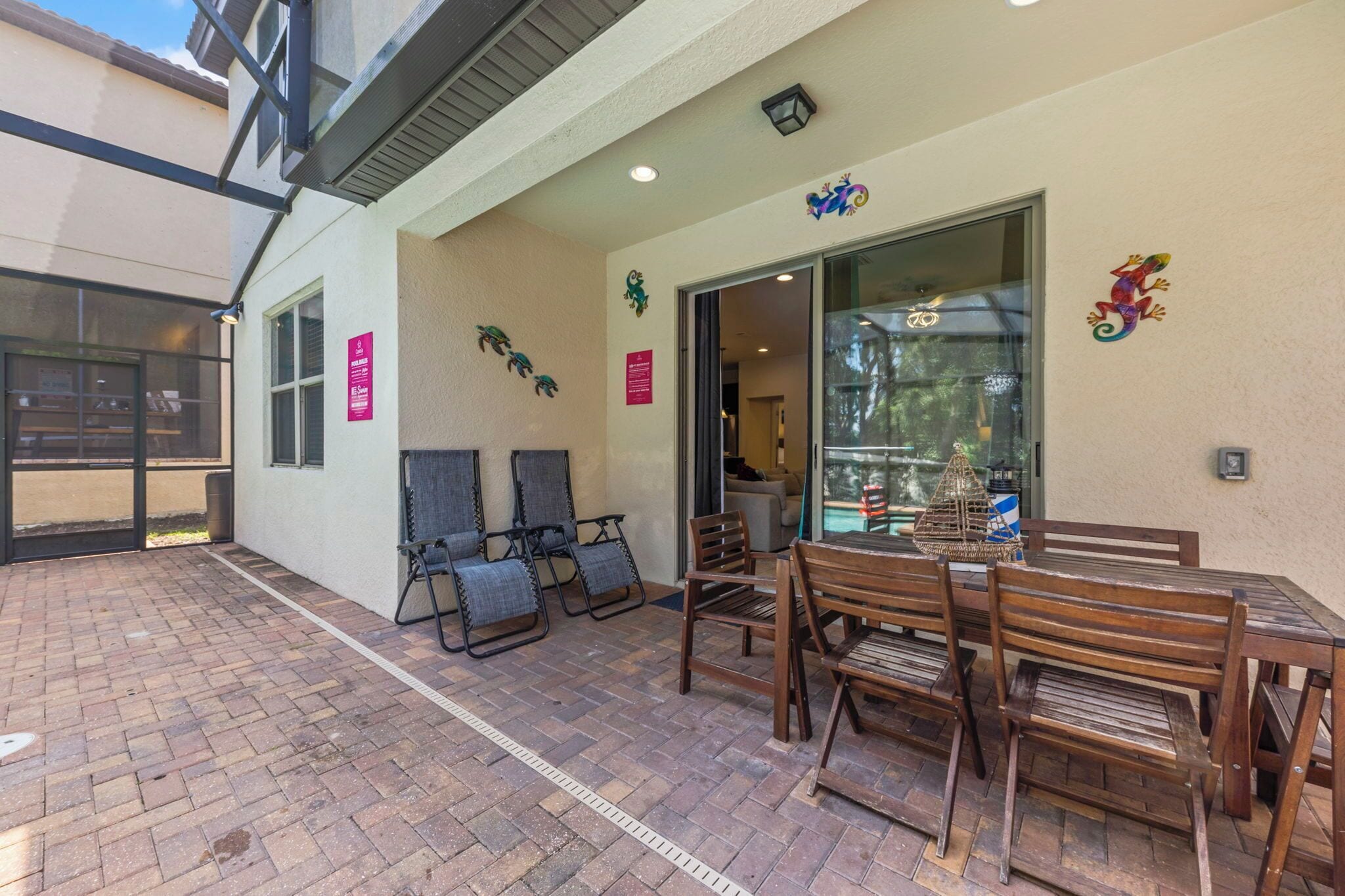 A patio area with brick flooring, wooden tables and chairs, and a glass door entrance.