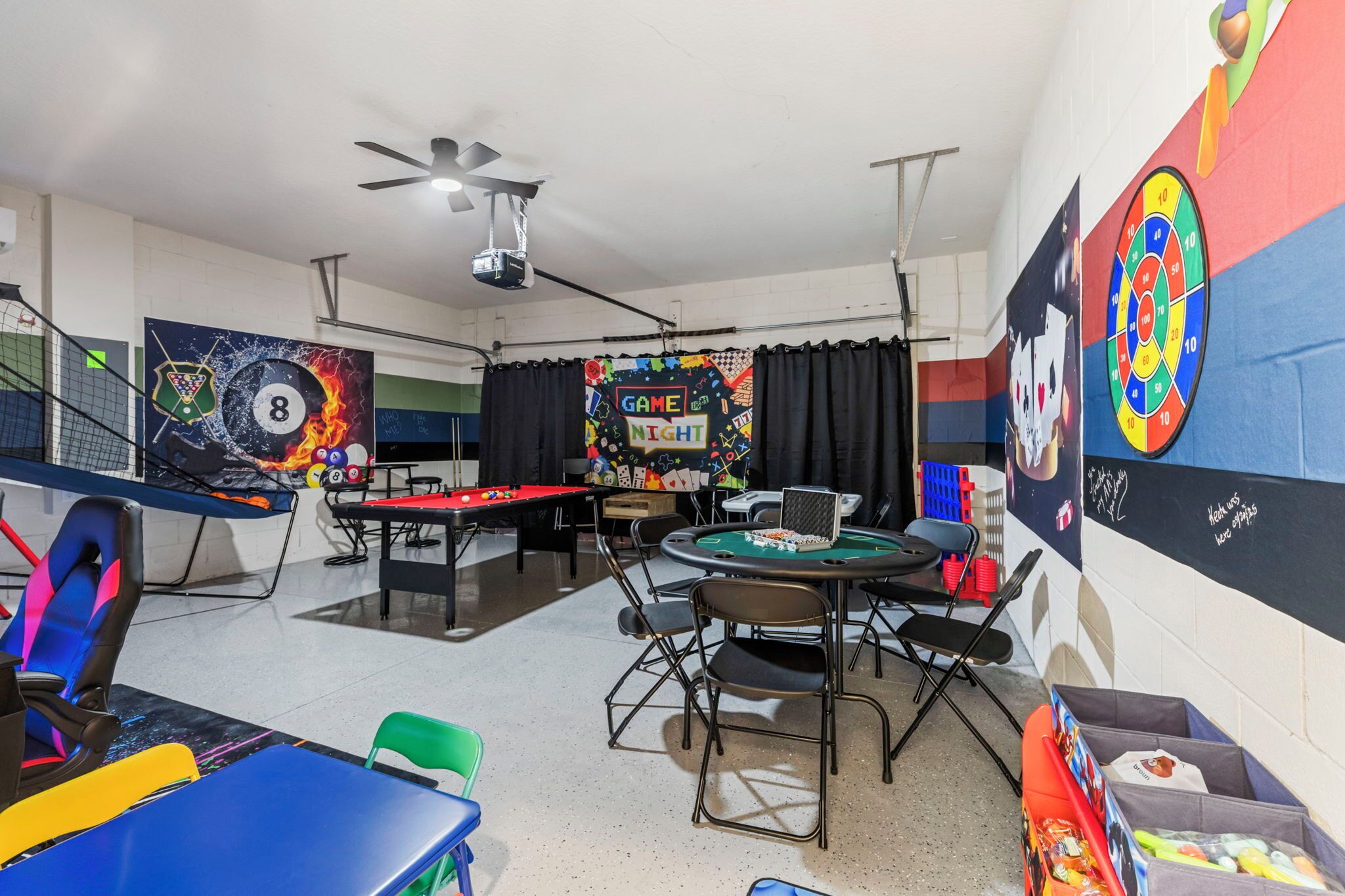 A gaming room with pool tables, chairs, and a dartboard.