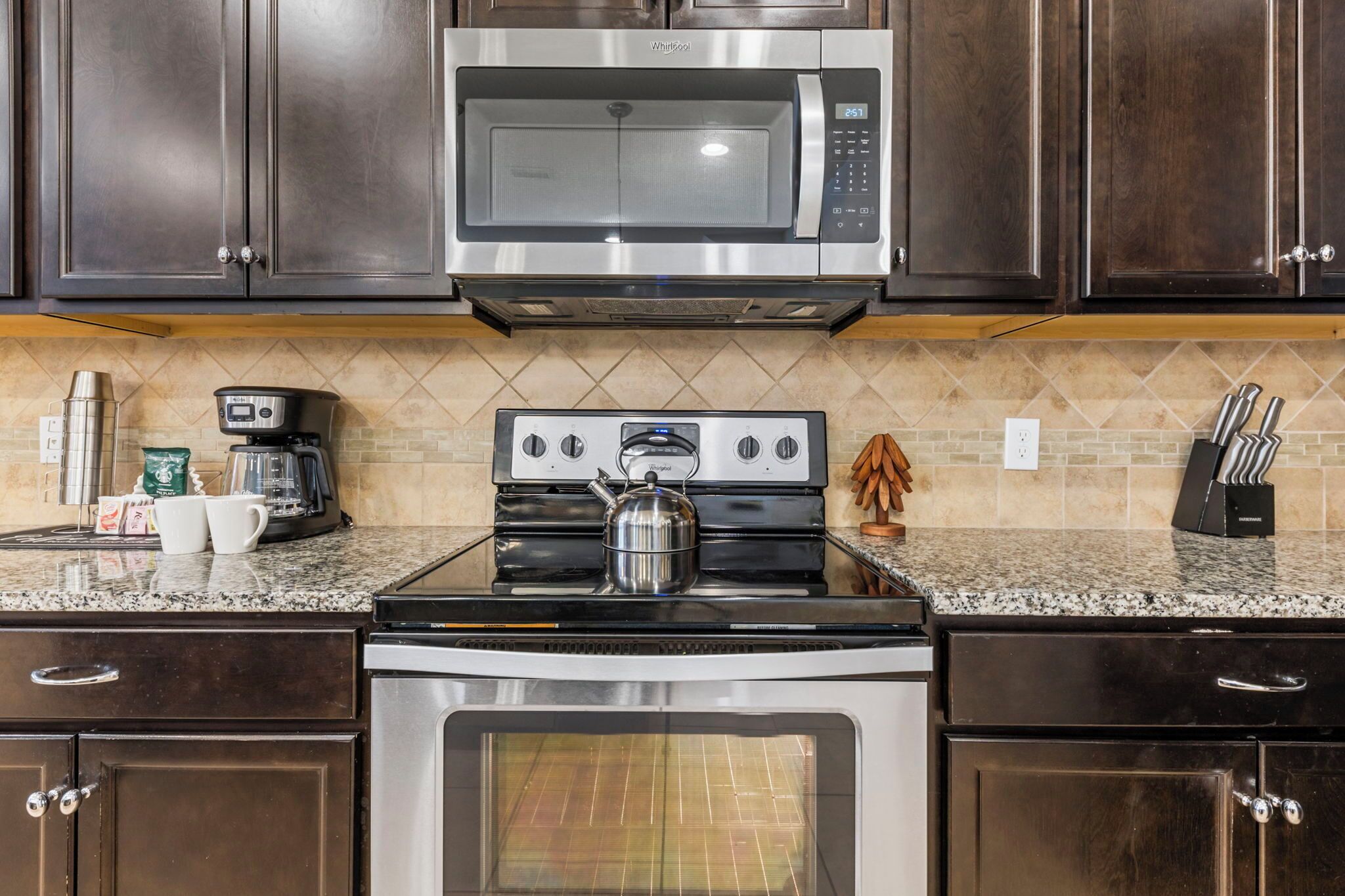 A kitchen with dark wood cabinets, a stainless steel microwave, a gas stove, and an oven.