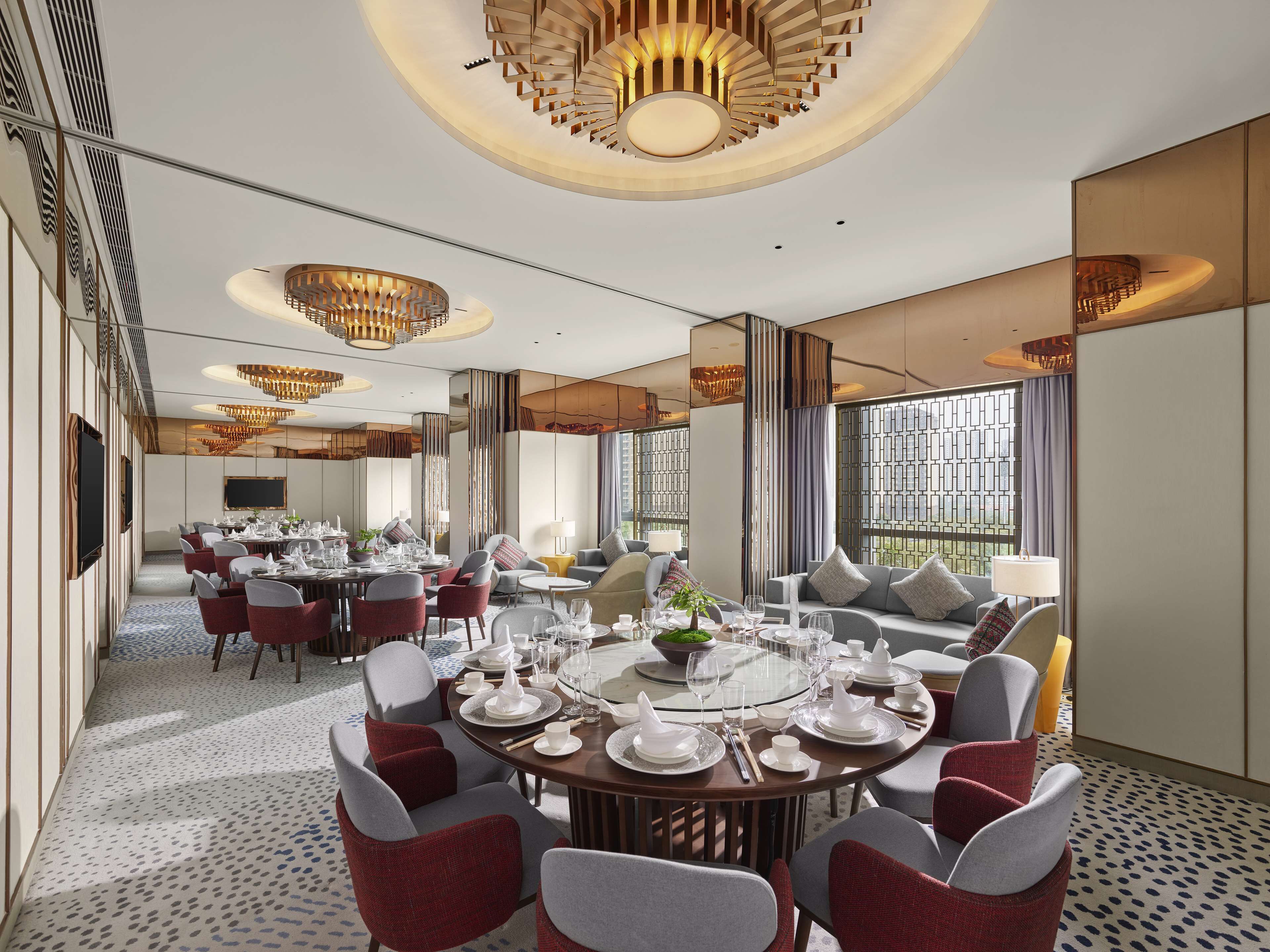 A modern dining area with round tables, red and grey chairs, and a large window with a view.