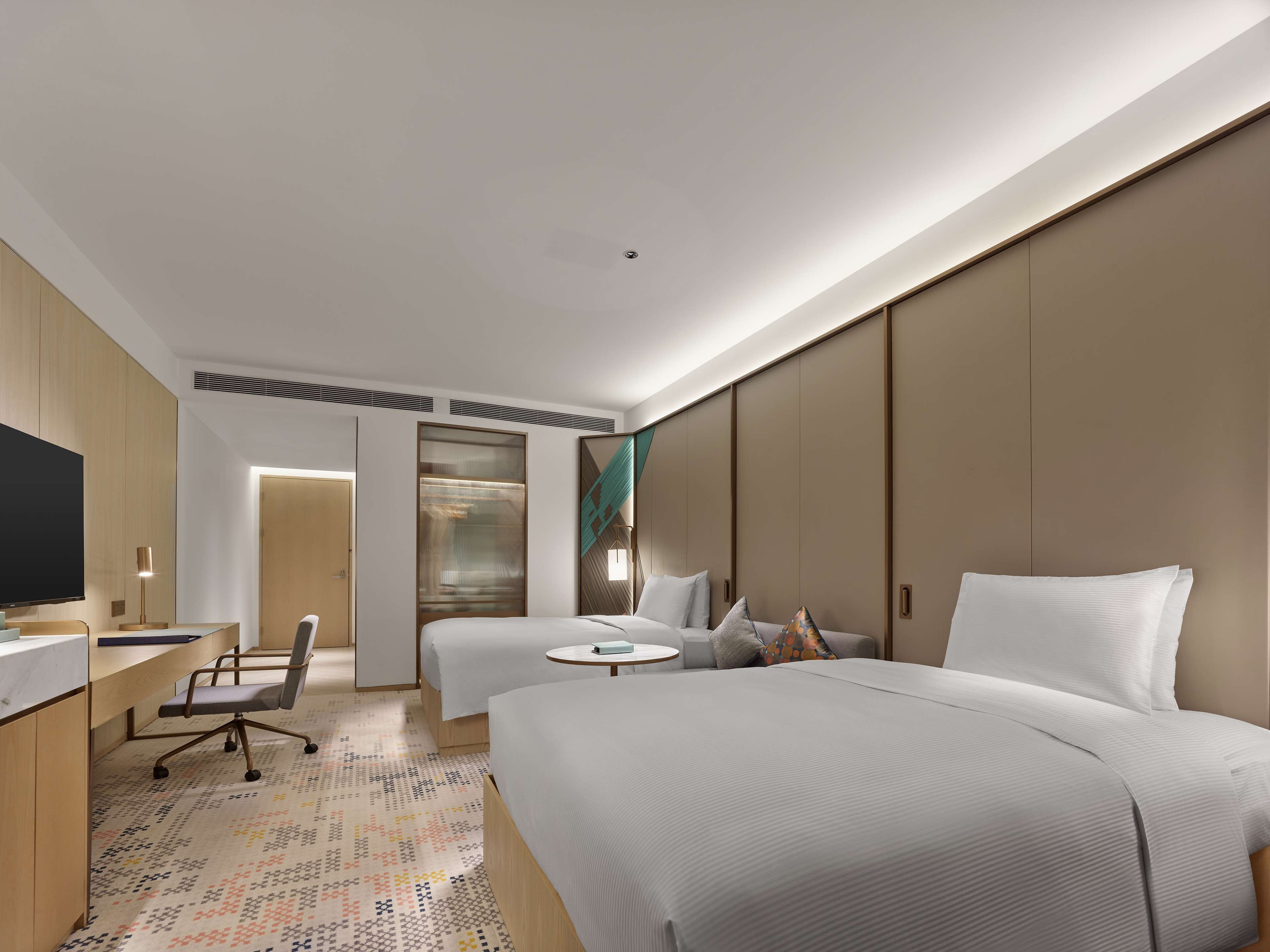 A hotel room with a large bed, a desk with a chair, a TV, and a patterned carpet.