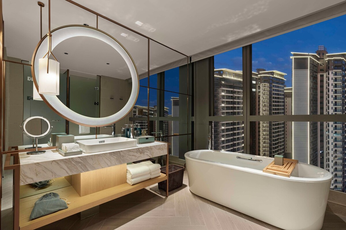A modern bathroom with a large bathtub, dual sinks, and a large mirror.