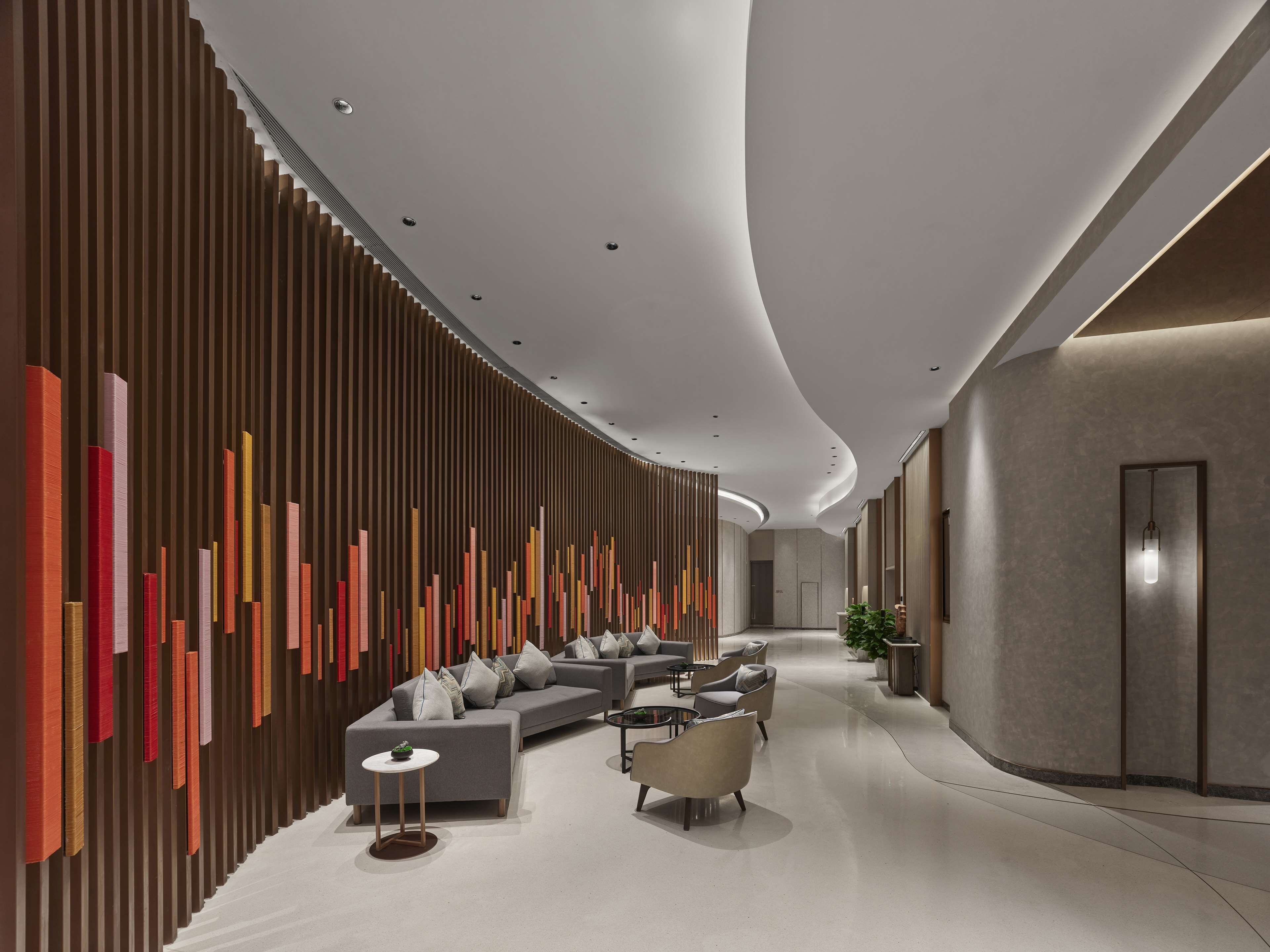 A modern hotel lobby with a curved ceiling, a sectional sofa, armchairs, and a small table.