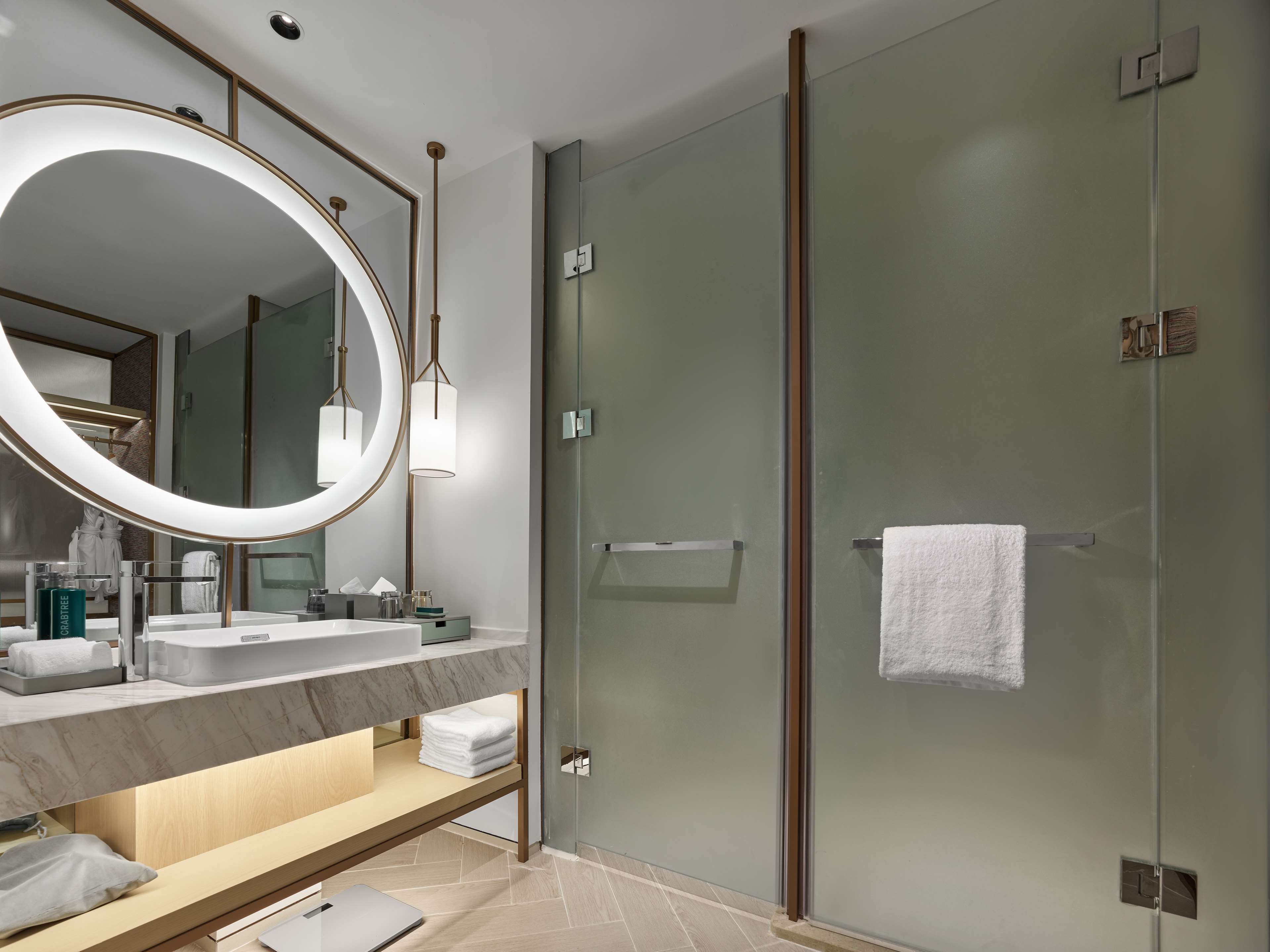 A modern bathroom with a large mirror, a glass shower enclosure, and a vanity with a marble countertop.