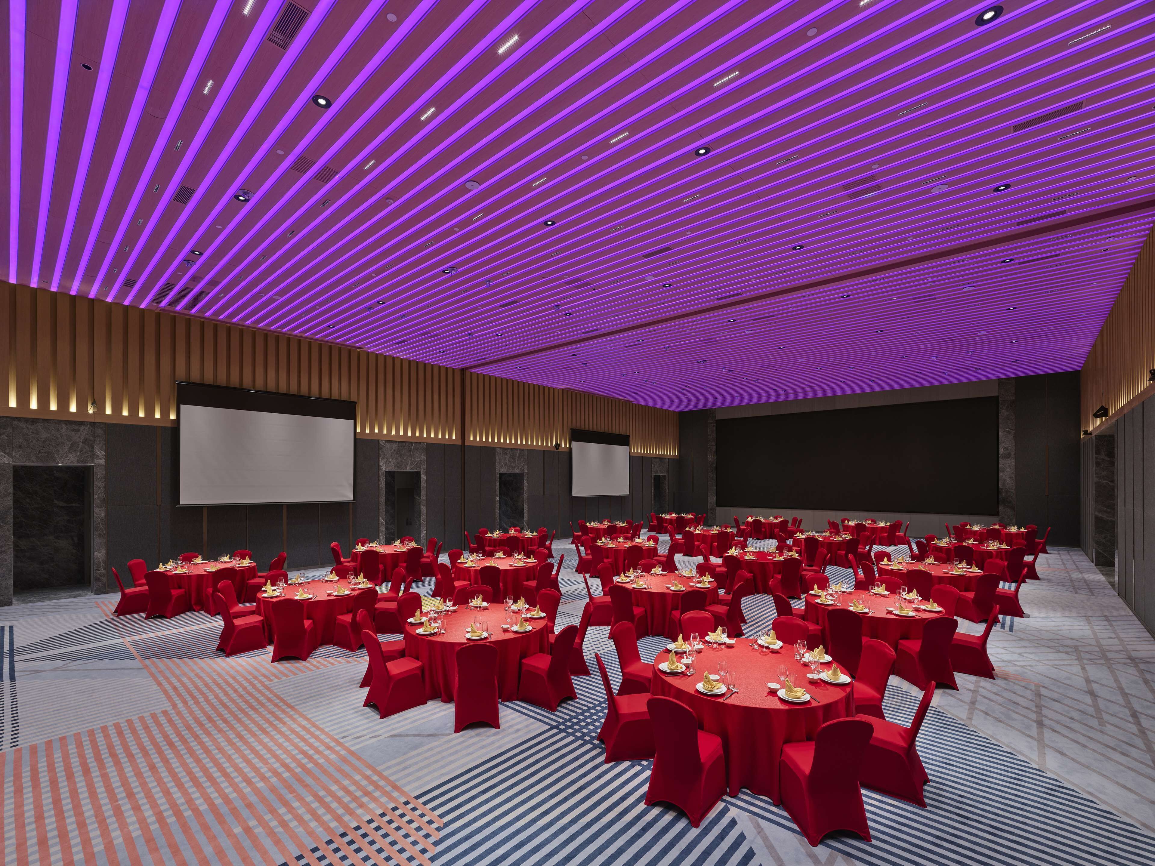 A conference room with multiple tables and chairs, equipped with screens and a modern ceiling design.