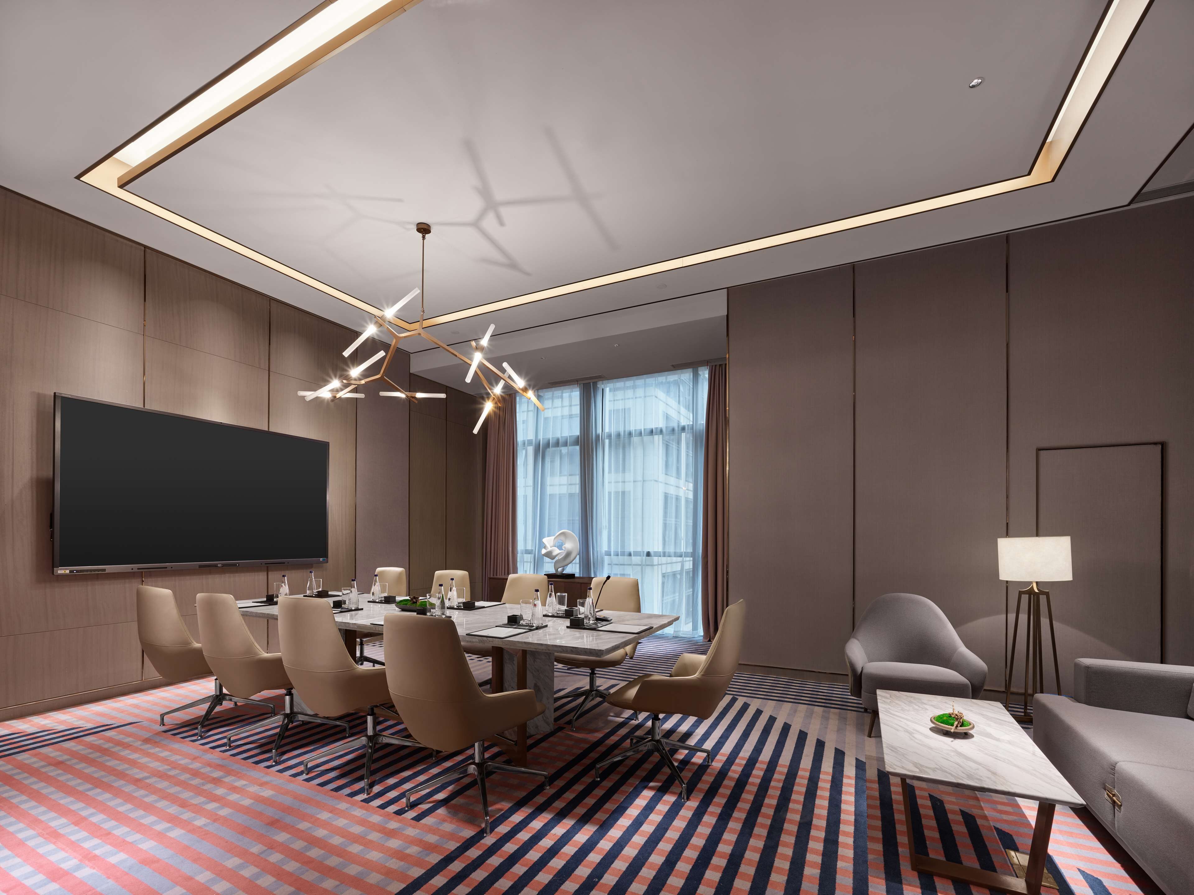A modern conference room with a large table, chairs, a flat-screen TV, and a patterned carpet.