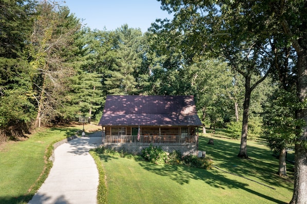 A cabin with a porch, surrounded by trees and a grassy area.