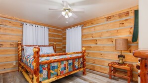 A wooden cabin bedroom with a bed, curtains, a ceiling fan, and a nightstand. - Valentine Drive Cabin 1 (Lookout Mountain)