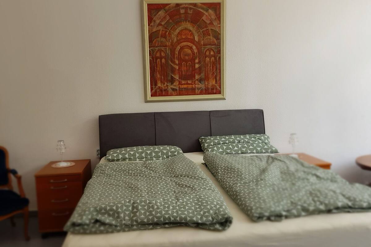 Ein Hotelzimmer mit einem Bett, zwei Kissen, einem Nachttisch, einem Sessel und einem Wandbild.