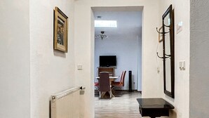 A hallway with wooden flooring, a radiator, a framed picture, a mirror, and a television in the background. - Apartment Fuchsbau (Senftenberg)