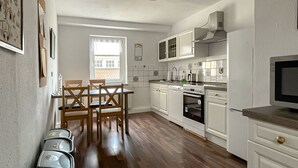 A modern kitchen with white cabinets, a dining table with chairs, and a built-in oven. - Apartment Fuchsbau (Senftenberg)