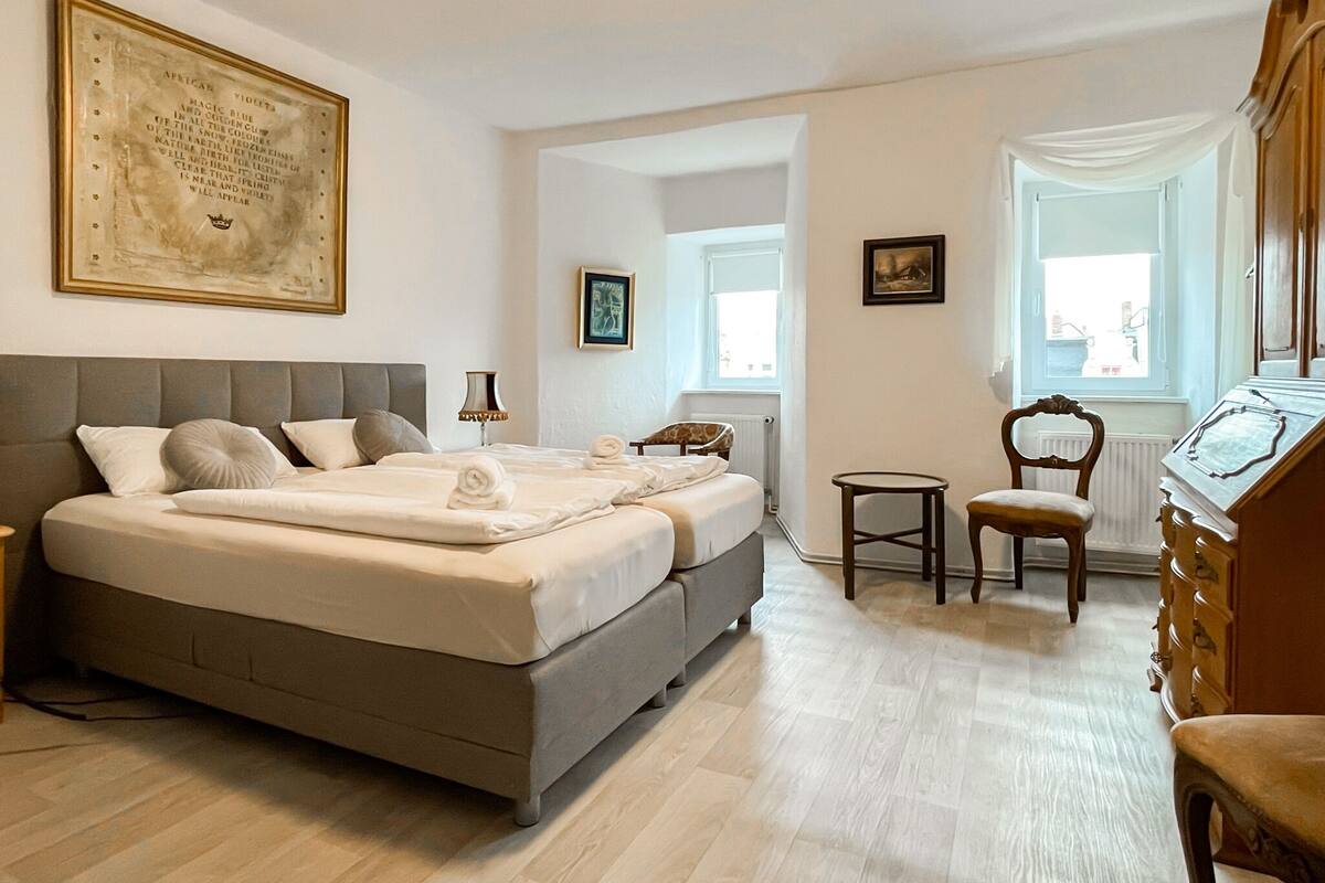 Ein Schlafzimmer mit einem großen Bett, einem Sessel, einer Kommode und einem Fenster.